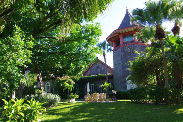 A large garden with palm trees surrounding a stone house with a tower.