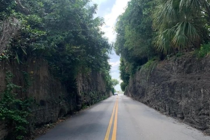 Narrow road through rocky and foliage-lined passage with clear sky above.