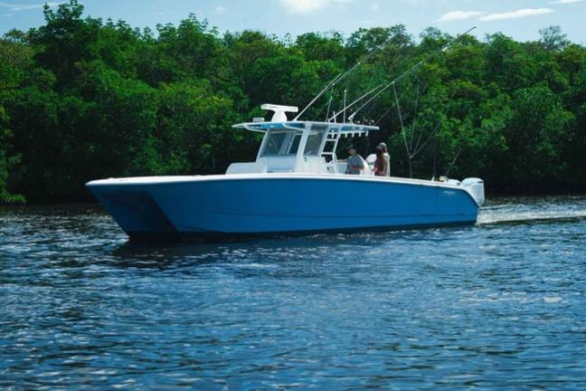 Blue boat with fishing rods on a lake, trees in the background under a blue sky.