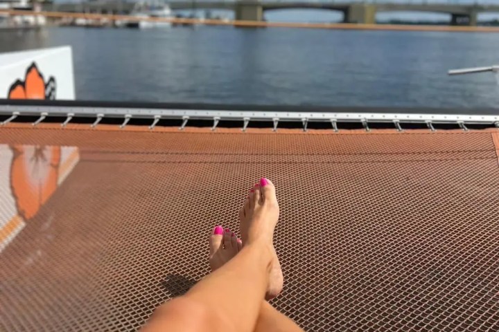 Person's legs on a boat netting with a bridge and water in the background.