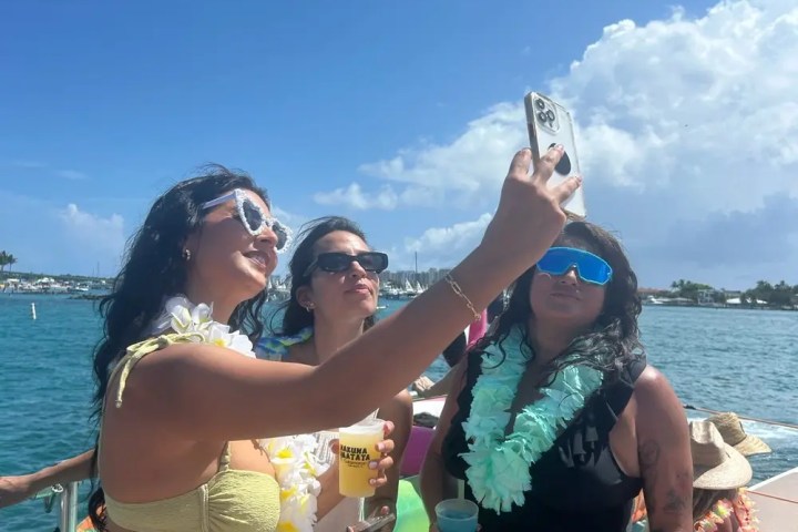 Three people on a boat taking a selfie under a clear blue sky.