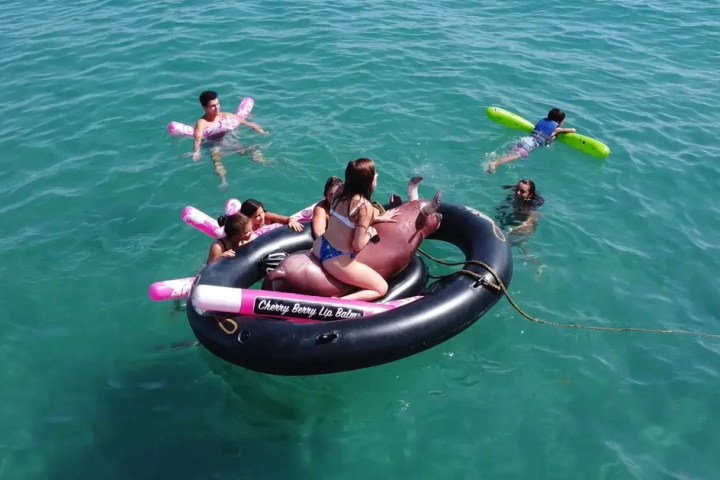 People enjoying water on inflatables, including a large black one with lip balm design.