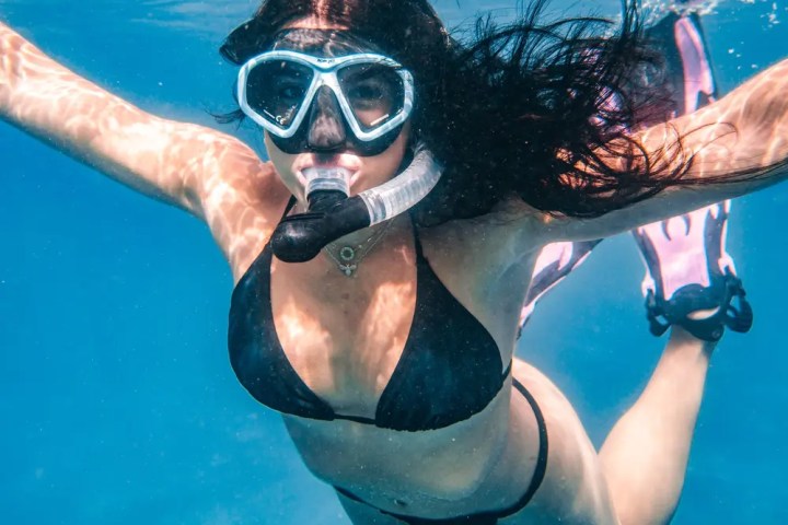 Woman snorkeling underwater in a black bikini, wearing goggles and a snorkel.