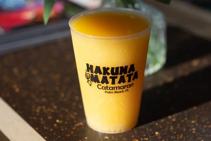 Tropical drink in branded cup on table, flowers in background.