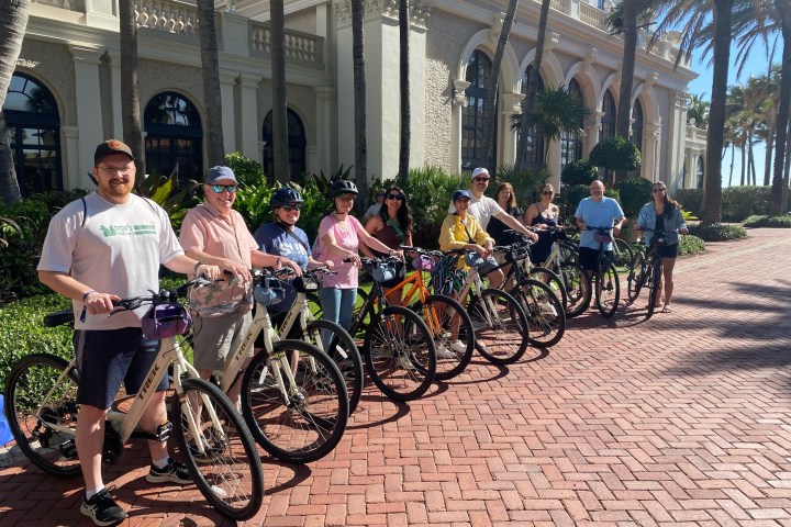 Group of people with bicycles lined up on a sunny brick pathway.