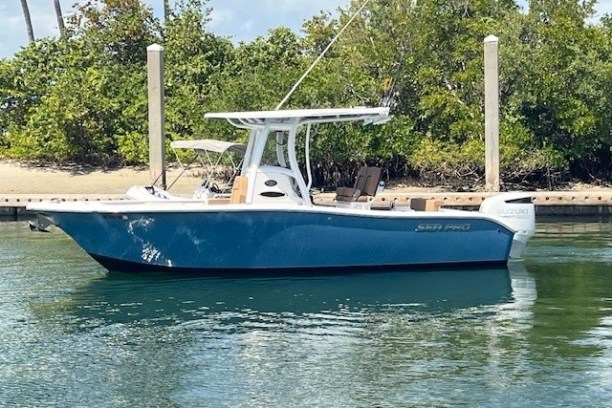 Blue and white motorboat docked on calm water near trees.