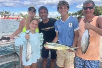 Group of five people smiling, holding fish by the waterfront.