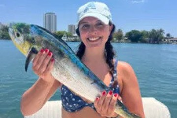 Woman on a boat holding a fish, wearing a hat and polka-dot swimsuit.