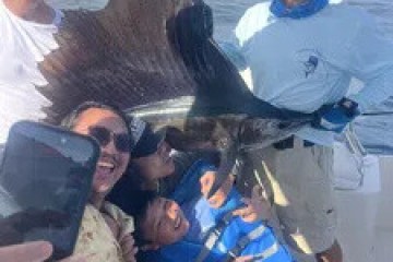 Group of people on a boat posing with a large fish and taking a selfie.