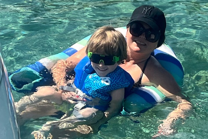 Adult and child in an inflatable float on clear water, both wearing sunglasses.