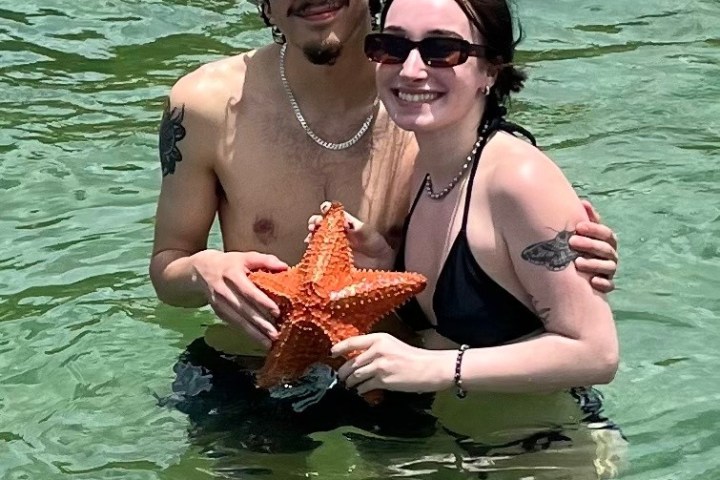 Two people in water holding a large starfish, both smiling and wearing sunglasses.