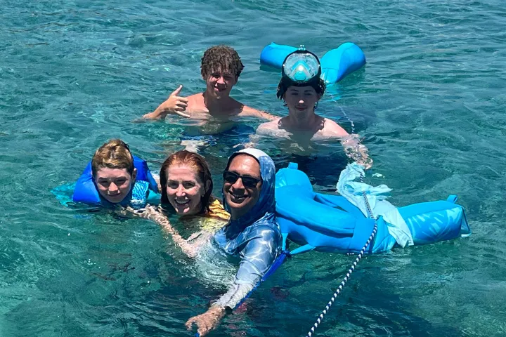 Five people smiling and floating in clear blue water with foam noodles.