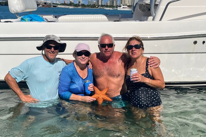 Four people in water with a starfish, standing near a boat.