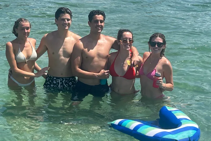 Five people in swimwear standing in clear ocean water with a float nearby.