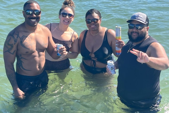 Four people standing in water, smiling and holding drinks.