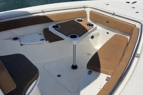 Boat deck with seating, table, cup holders, and calm water in the background.