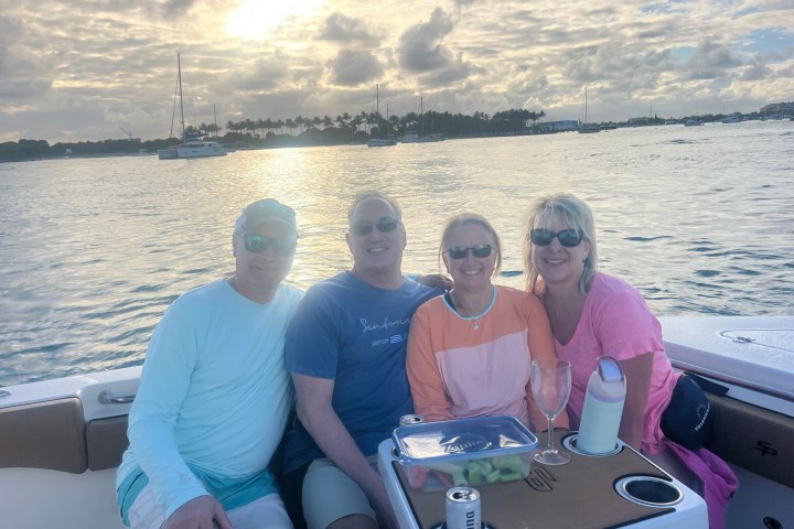Four people seated on a boat at sunset with snacks and drinks.