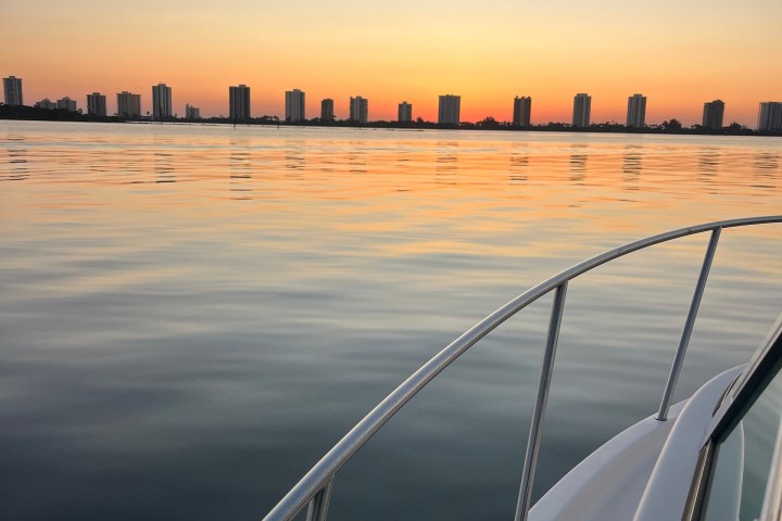 Boat on calm water at sunset with city skyline in the distance.