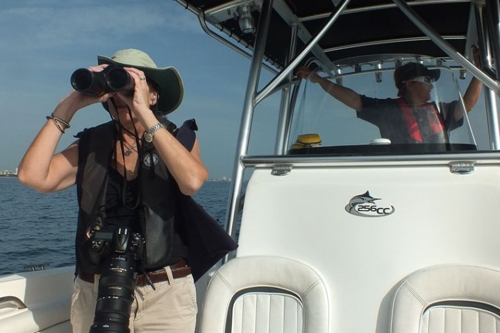 Two people on a boat; one using binoculars, the other steering.
