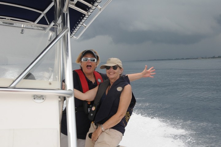 Two people on a boat smiling with stormy skies in the background.